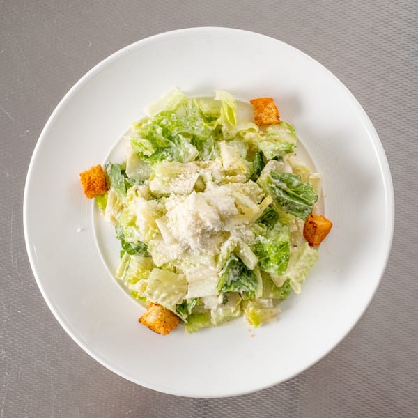 Caesar salad with crisp lettuce, creamy dressing, golden croutons, and grated Parmesan on a white plate.