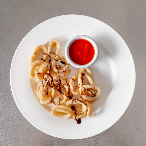 Fried calamari rings with a red dipping sauce and dark glaze on a white plate.
