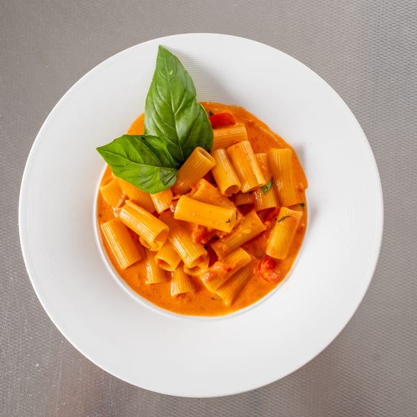 Rigatoni pasta in a creamy orange sauce with fresh basil and cherry tomatoes.