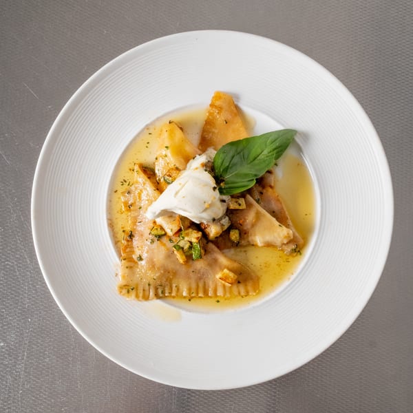 Triangular pasta in a light sauce with cream, basil, and diced vegetables on a white plate.