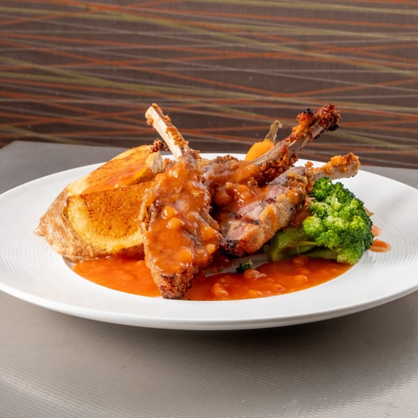 Two lamb chops with bean sauce, broccoli, and a golden side on a white plate.