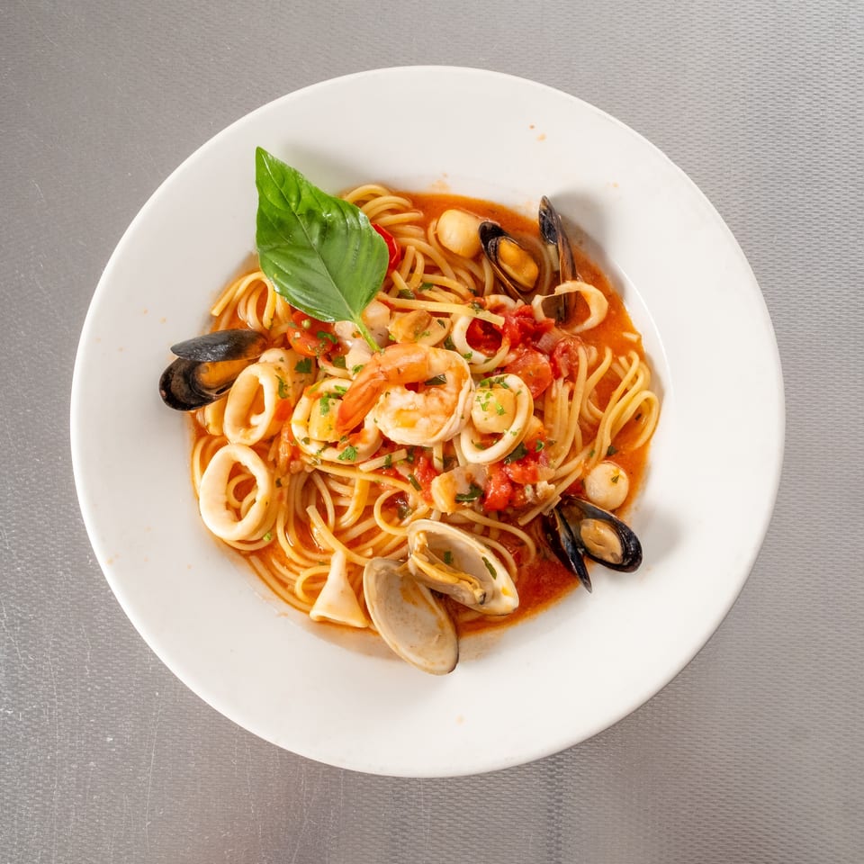 Seafood spaghetti with shrimp, mussels, clams, calamari, and scallops in tomato sauce, garnished with basil.