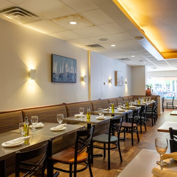 Well-lit restaurant interior with rows of set tables, booth seating, and sailboat artwork on the walls.