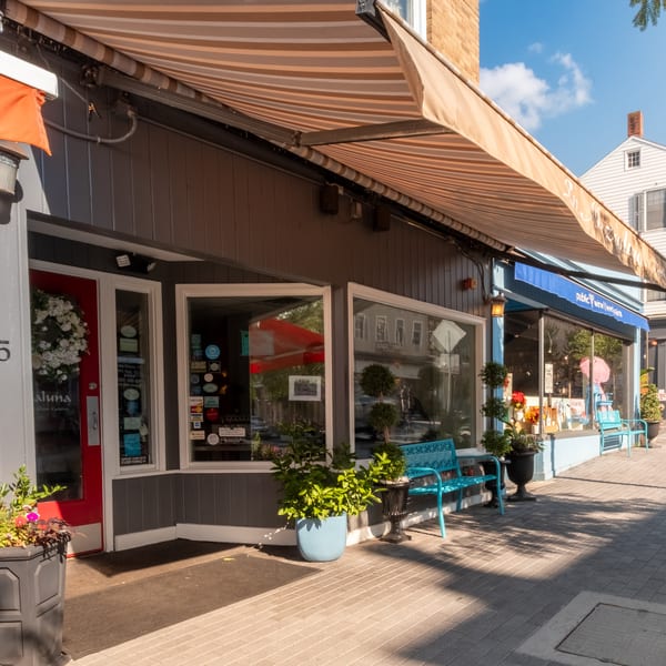 Aluna Italian Cuisine storefront with a red door, striped awning, and outdoor seating on a sunny sidewalk.
