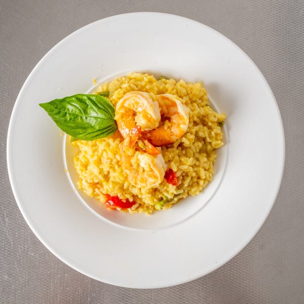 Plate of creamy yellow risotto with three cooked shrimp, fresh basil, and diced tomatoes.