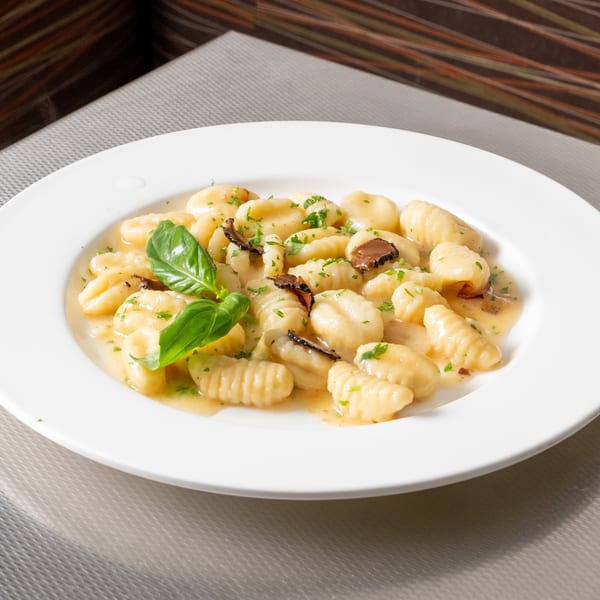 Gnocchi with truffle shavings, basil, and parsley in a light sauce on a white plate.