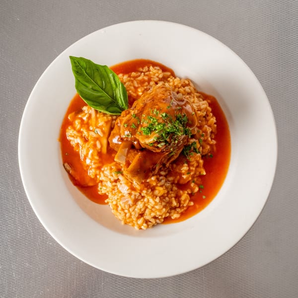Braised meat shank over rice in tomato sauce, garnished with parsley and basil.