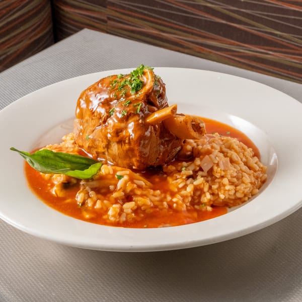 Osso buco with creamy tomato risotto and fresh basil on a white plate.