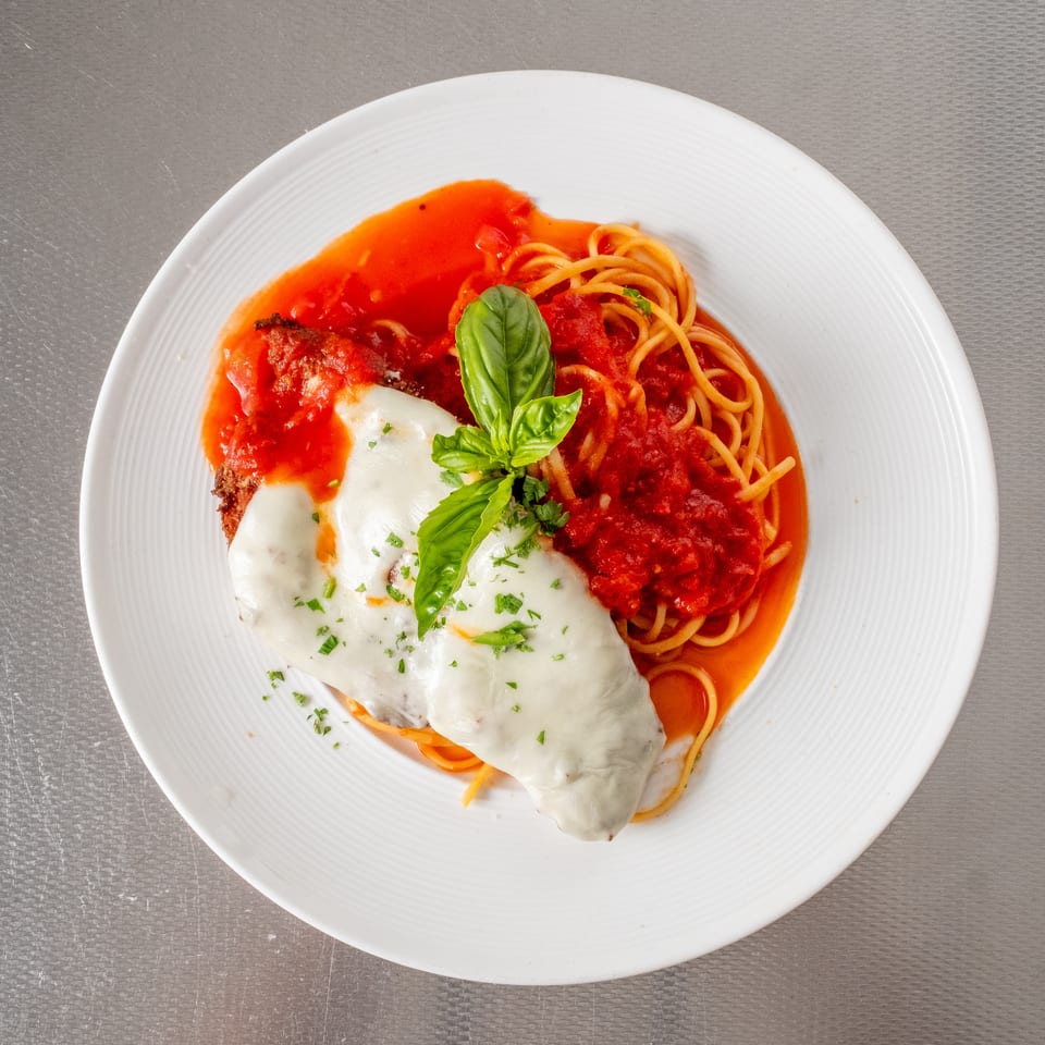 Chicken Parmesan with spaghetti and red sauce, garnished with fresh basil.