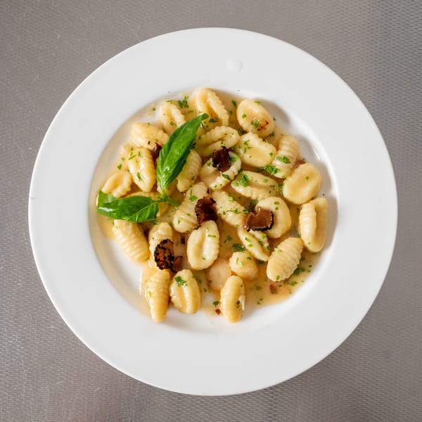 Gnocchi with truffle shavings, basil, and parsley in a light sauce on a white plate.