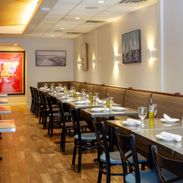 Long, empty restaurant dining room with set tables, booth seating, and warm wall lighting.