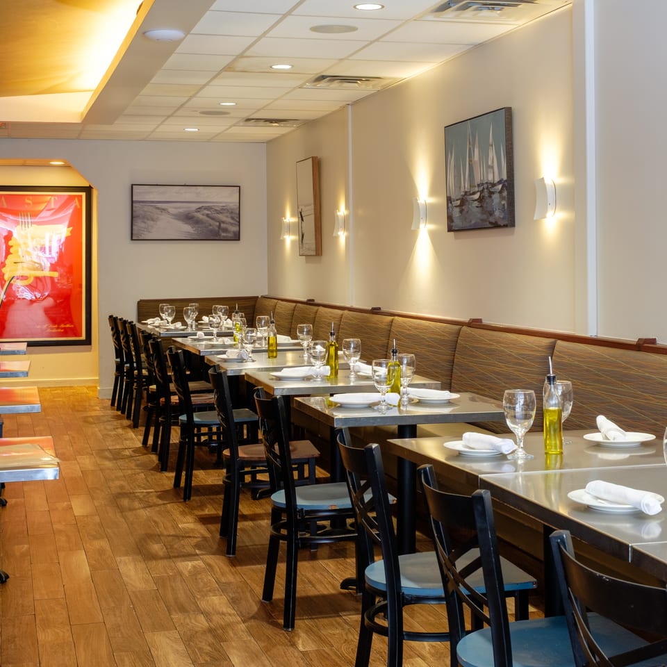 Long, empty restaurant dining room with set tables, booth seating, and warm wall lighting.