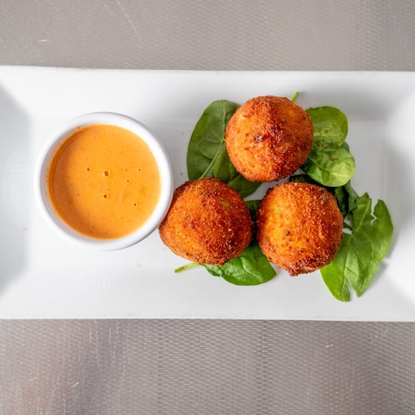 Three golden-brown fried balls with spinach and orange dipping sauce on a white rectangular plate.