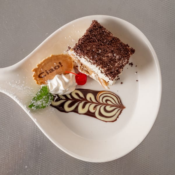 Elegant tiramisu dessert with chocolate, whipped cream, cherry, mint, and a 'Ciao!' cookie.